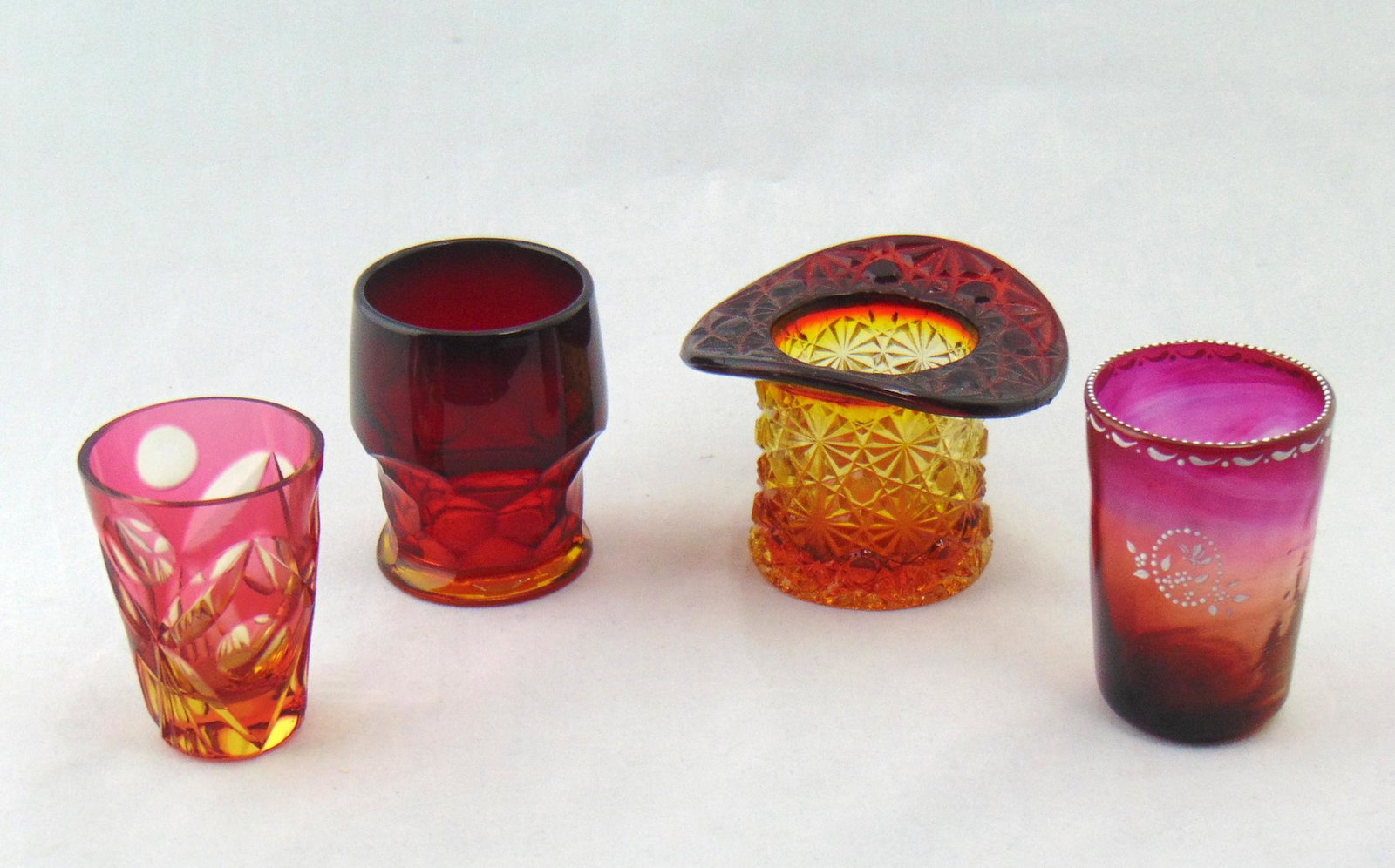 Toothpick - Four Cranberry: Four cranberry glass toothpicks including a ruby cut to ambergris, a daisy and button hat, an enameled cranberry and a faceted Amberina, tallest 2 3/4" ht. Condition: good with no defects found
