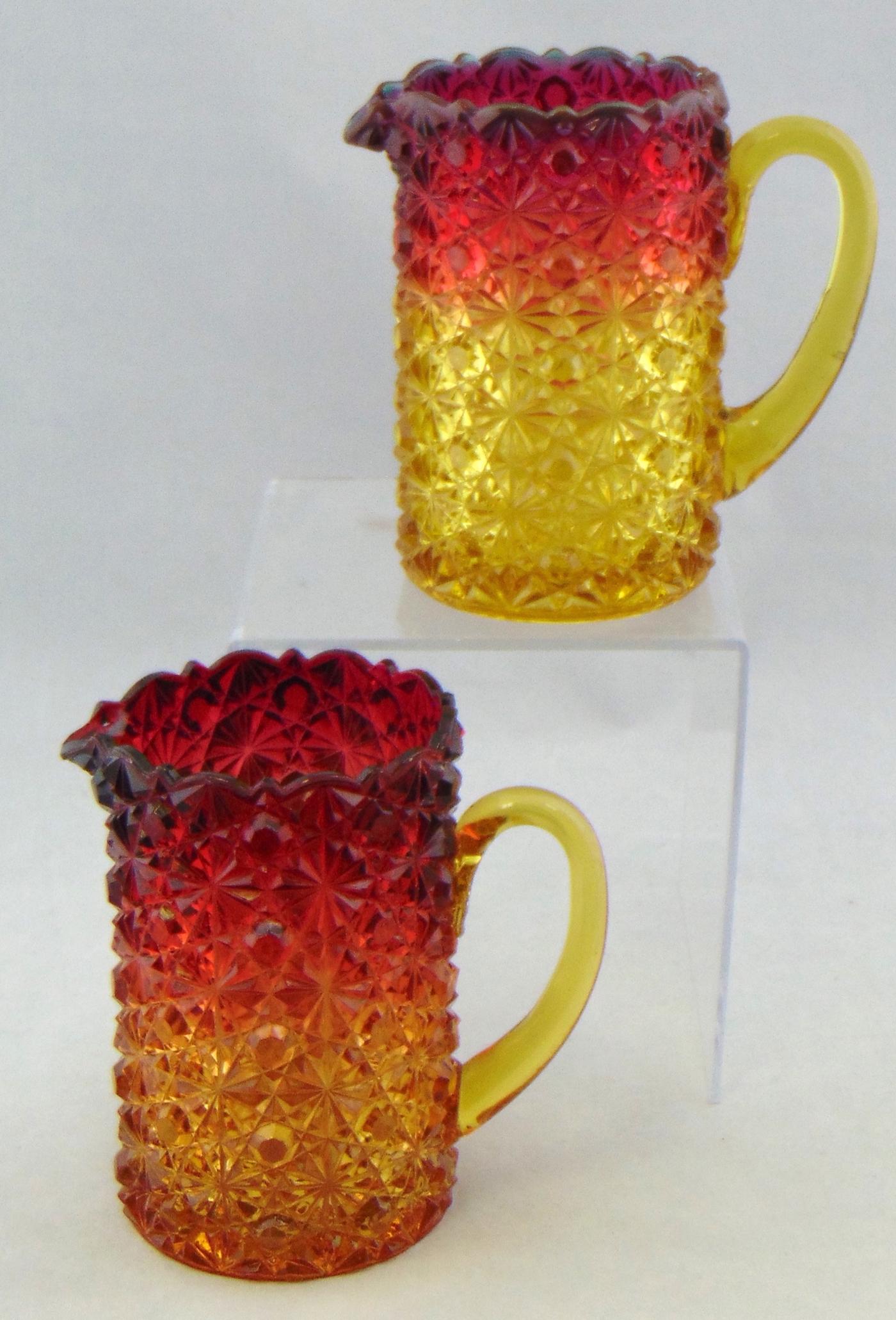 Two Hobbs pressed Amberina pitchers: Medium size pitchers in the daisy and button pattern, 5" ht. Condition: one with what appears to be a heat check at the side of the handle but does not extend to the back.