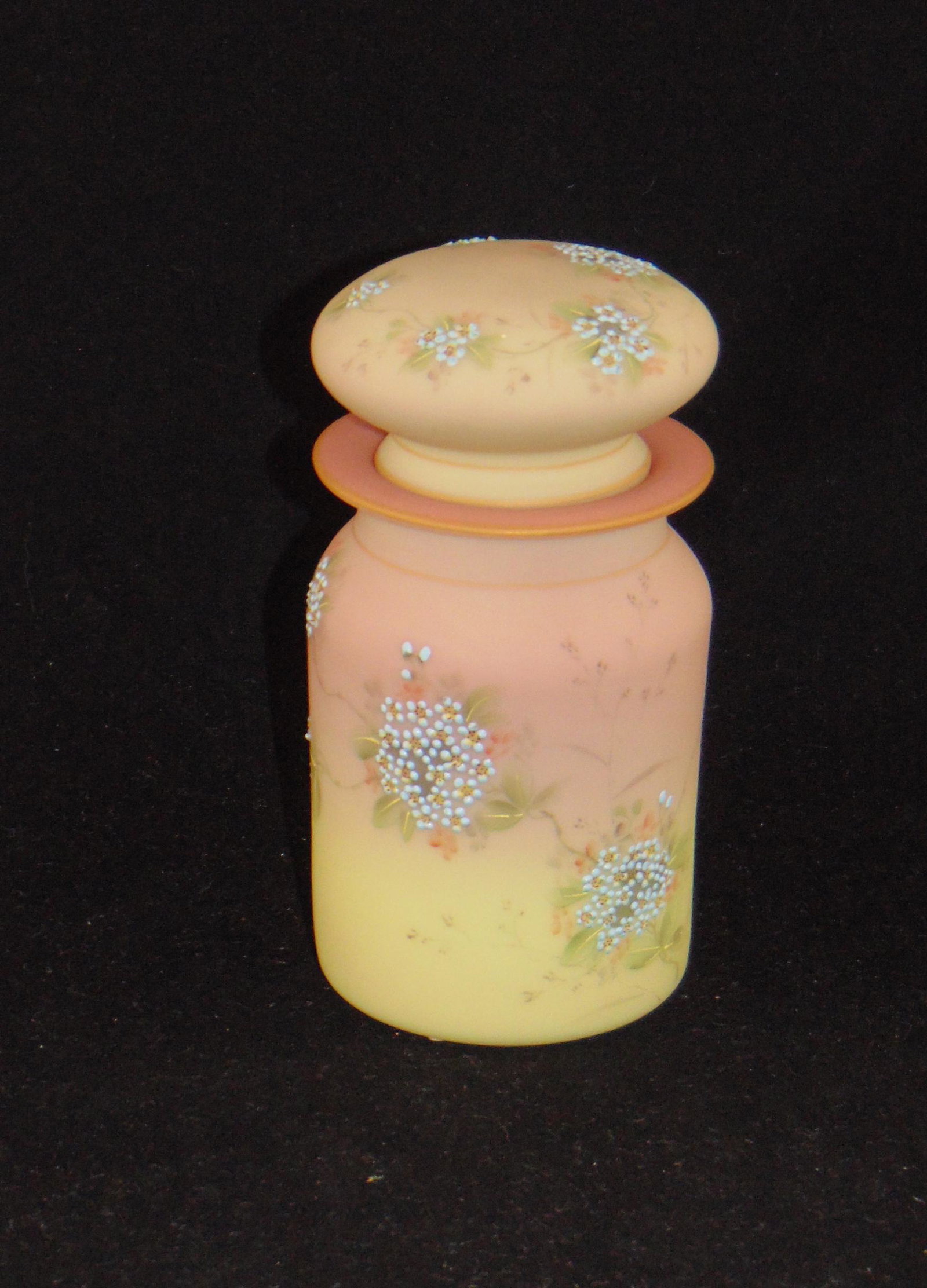 Mt. Washington covered dresser Jar: Mt. Washington Burmese covered dresser Jar, cylindrical form in cream to pink decorated with clusters of blue daisies, fitted with a matching stopper, 6" ht. PROVENANCE: Earlys Auction to the black co