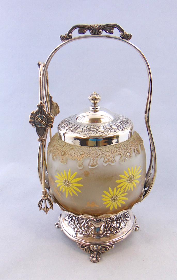 Royal Flemish glass pickle castor: Mt. Washington ovoid glass jar with raised coral design borders decorated with yellow mums set in a four footed signed Pairpoint silver plate holder, 9 1/2' ht. Condition: good with no defects found.