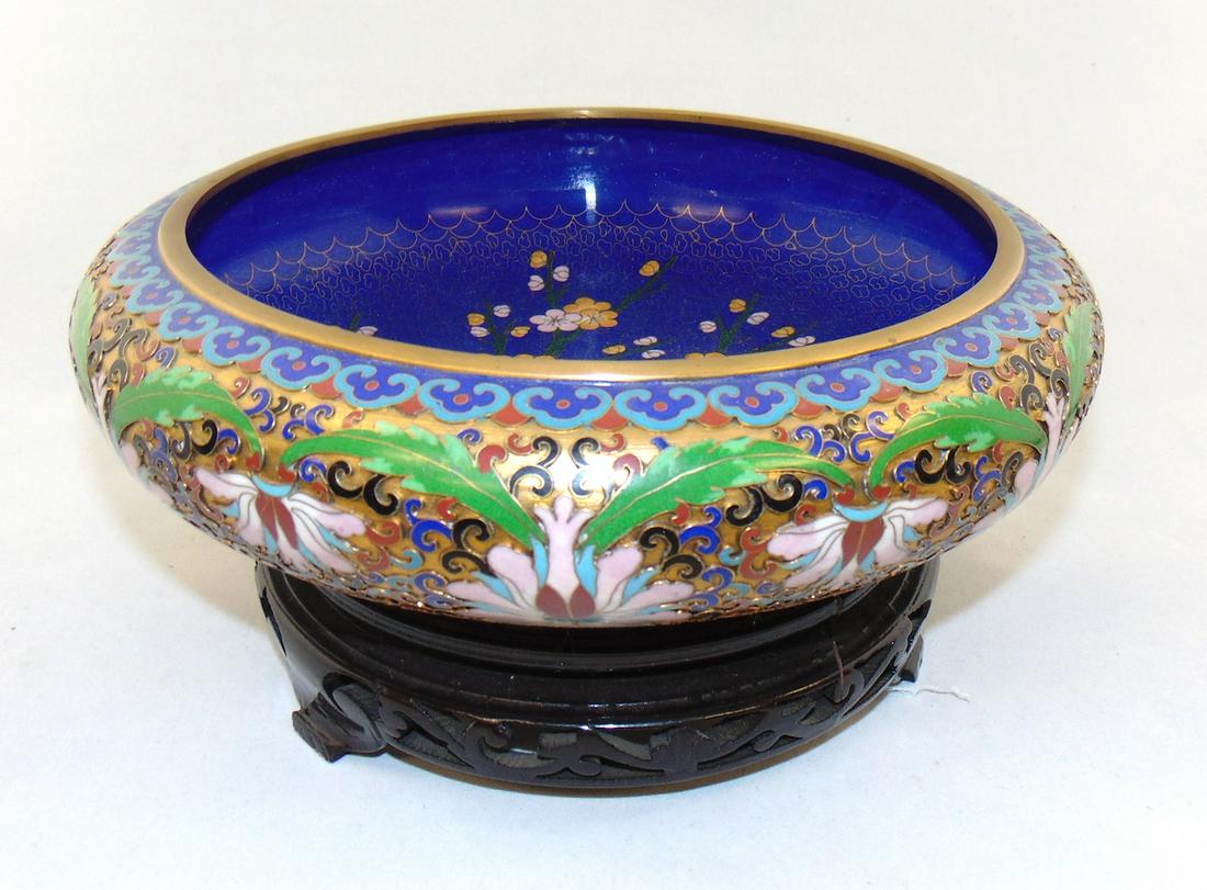 Cloisonne bowl on stand: Cloisonne enamel on copper bowl with pink flowers and red and blue scrolling set on a wood base, 7 1/2" wide. Condition: good with no defects found.