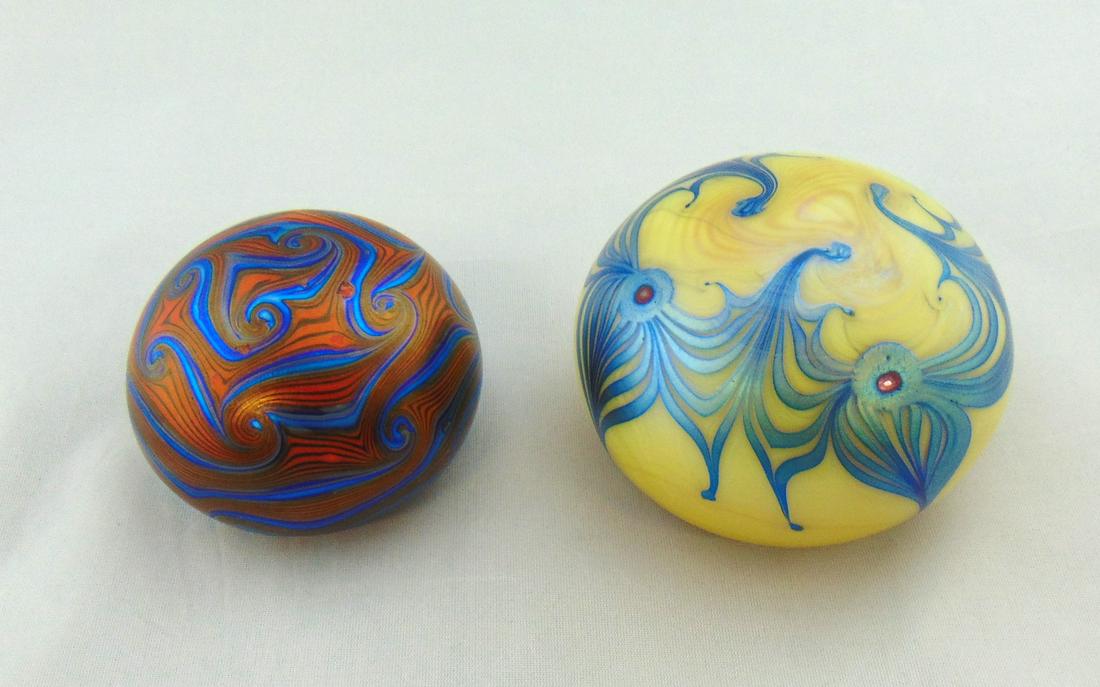 Two Orient and Flume Paperweights: Two iridescent Orient and flume paperweights, one in opal with red peacock eye on blue feathers, together with a deep crimson with blue hooked feather, both signed 76 and 75, 3 1/4" wide. Condition: g