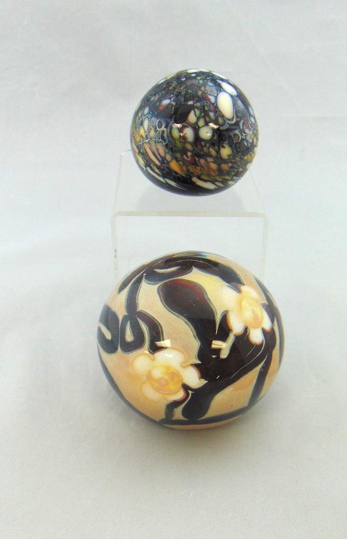 Two Jay Byron glass Paperweights: Two Jay Byron glass paperweights one with multi colored spatter the larger in tan with white flowers on crimson vines, each signed J Byron, largest 3" wide. Condition: good with no defects found.