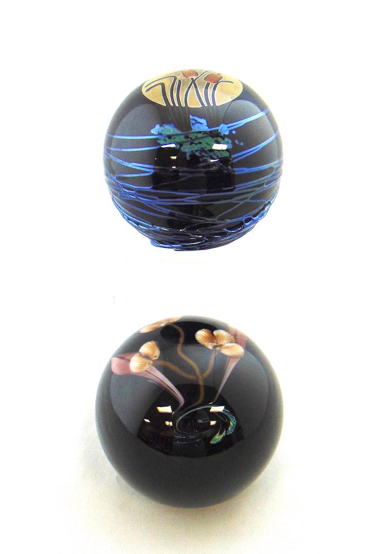 Two Rick Satava Studios Paperweight: Dark blue paperweights one decorated with a medallion of cat tails the other with a single stem flower, both signed Satava, 3" wide. Condition: good with no defects found.