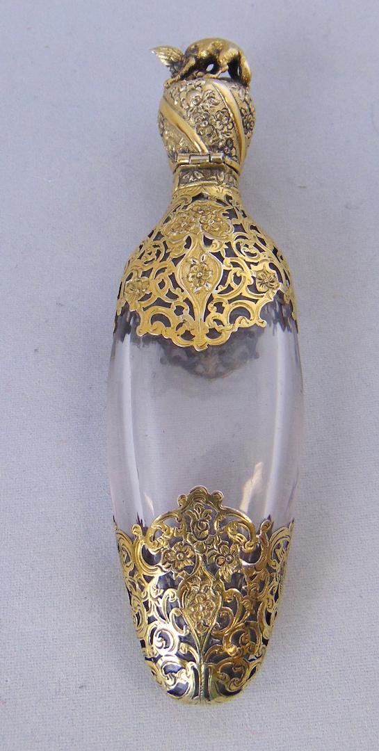 Glass and reticulated metal perfume: Tear drop form in clear glass decorated with reticulated scrolling metal foot and lid with a fighting wolf and bird finial, internal stopper of a wolfs head, 4 1/2" long. Condition: good with no defec
