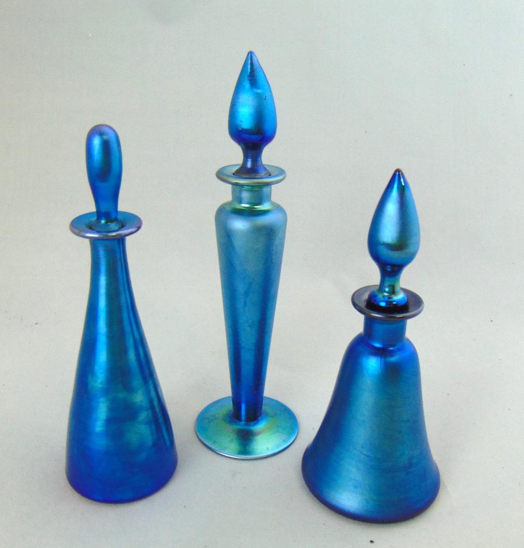 Three Steuben Blue Aurene bottles: Including a 1414 cylindrical, a tee pee shape 3294, and a conical cologne bottle shape number 1818, tallest 7 1/2' ht. Condition: good with no defects found