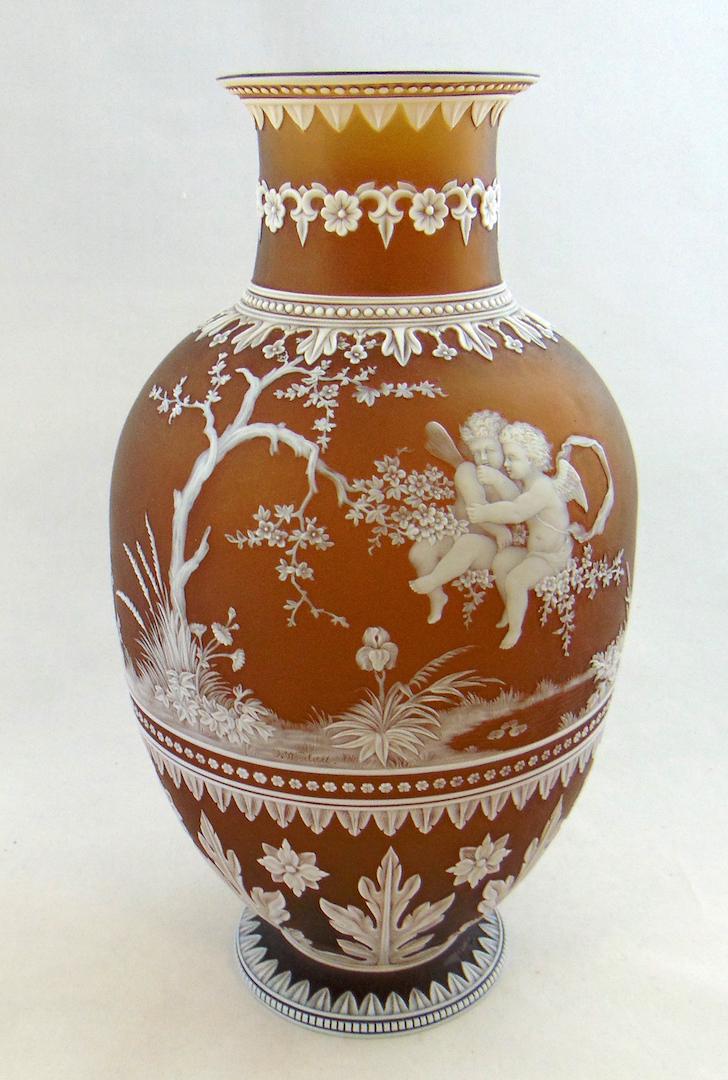 Thomas Webb and Sons Woodall vase: Footed urn form in dark umber glass decorated with two cherubs in a tree hovering over a garden pond, reverse with single figural cherub on a vine framed with multiple bands of arrow points, acanthus