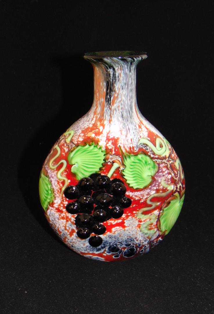 Orient and Flume glass vase: Bottle form in mottled red glass decorated with applied purple grapes on green leafy vines, signed Alexander/Smallhouse, 8" ht. Condition: good with no defects found.