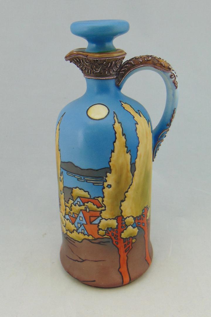 Nippon scenic porcelain jug: Cylindrical form with stopper and handle decorated with a blue and brown scene of a lake town under a full moon sky, marked Nippon, 11" ht. Condition: good with no defects found.
