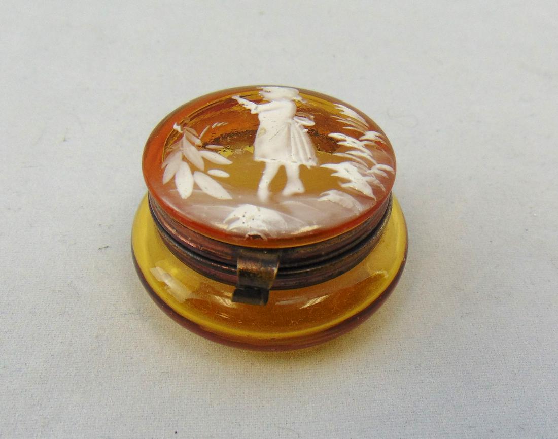 Mary Gregory glass pill box: Ovoid amber pill box with Mary Gregory child, 1 1/2' wide. Condition: good with no defects found.