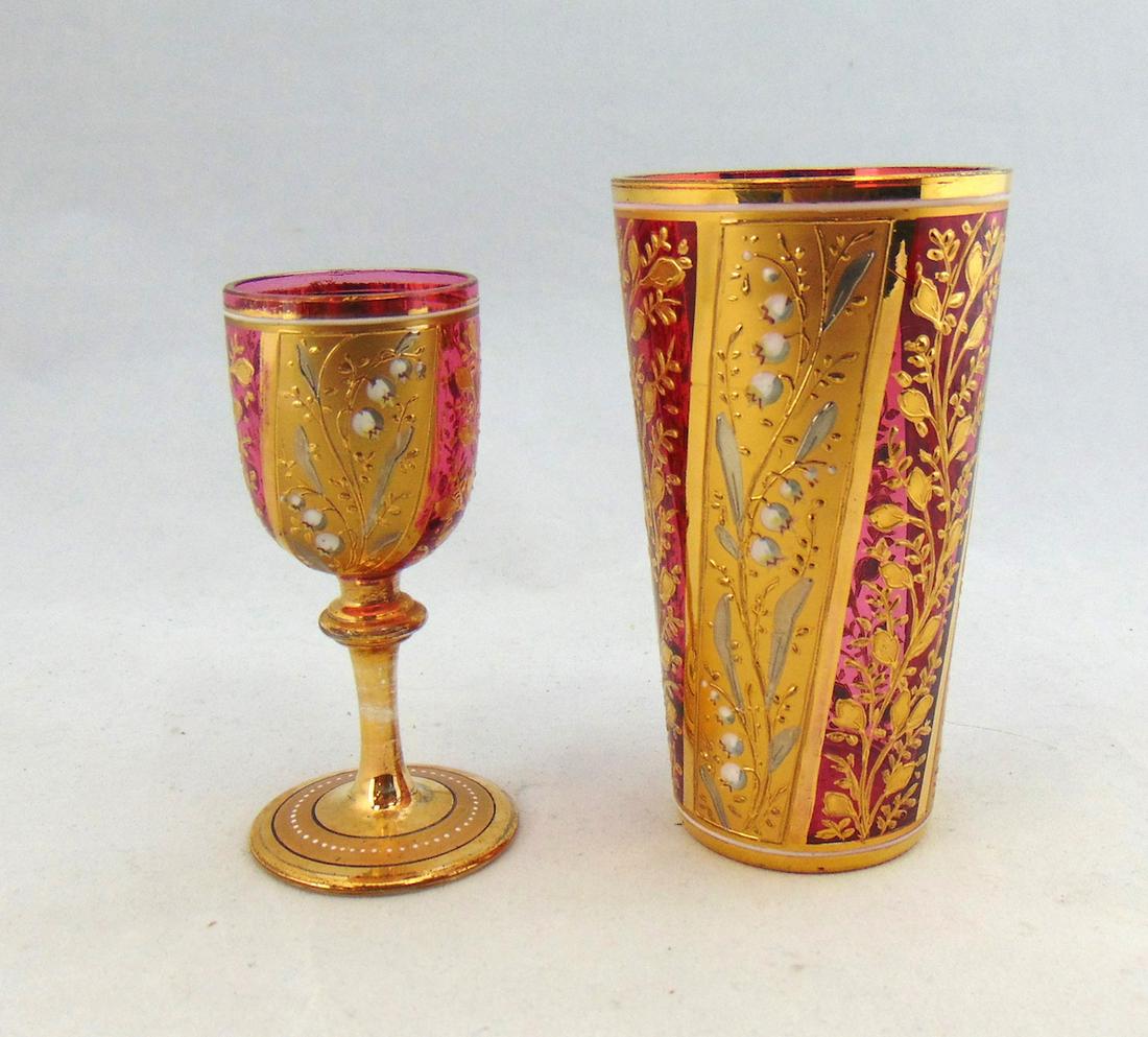 Two cranberry Moser glass items: Including a tumbler and diminutive goblet with exact dÃ©cor of alternating gold scrolling and gilt panels with bell flowers, tallest 3 3/4" ht. Condition: good with no defects found.