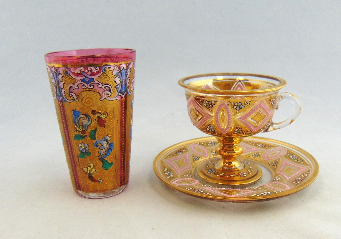 Two Moser gilt glass items,: Including a gilt panel tumbler with polychrome scrolling together with a gilt cup and saucer with flowers and pink geometric shapes, tallest 3 3/4" ht. Condition: good with no defects found