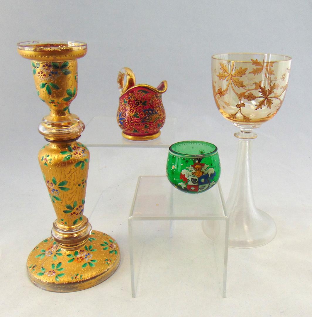 Four piece grouping of Moser: Including a gilded candlestick with overall flowers, a diminutive cranberry pitcher with deco design a green neo-Renaissance cordial and a goblet, tallest 7 3/4' ht. LITERATURE: "Moser Artistry in Gla