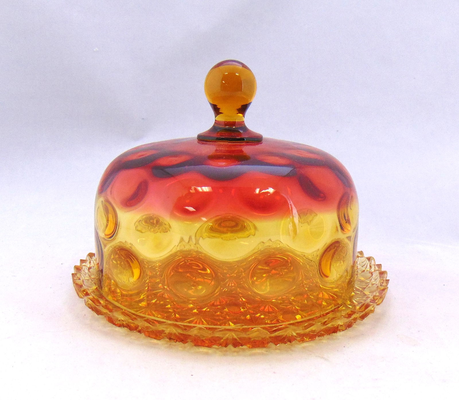 Hobbs Amberina covered butter dish: Amberina doom covered butter in the coinspot pattern set on an amber daisy and button tray, 7" wide. Condition: minor roughness to the teeth of the tray, see picture.