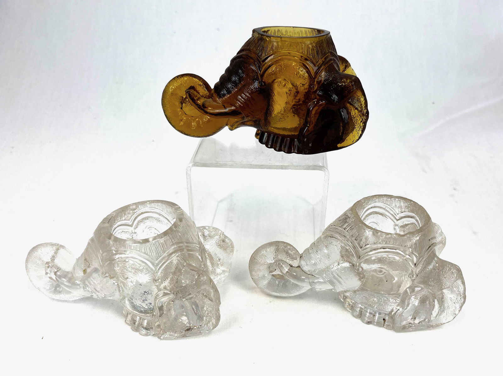 Three Findley Elephant head toothpicks: Three old Findlay elephant head toothpick holders two clear and one amber, 4 1/2" long. Literature: Bredehofts/the Sanfords - Glass Toothpick Holders, Second Edition, p. 77. CONDITION: chips to the ri