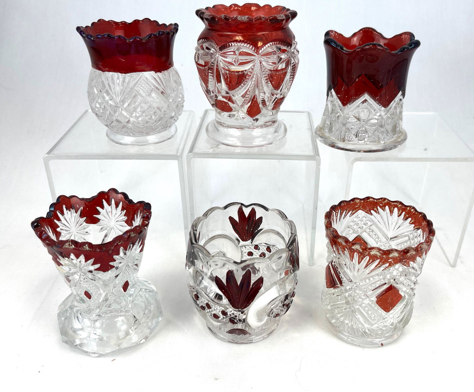 Six ruby stained toothpick holders: Six EAPG ruby stained toothpick holders including a Riverside Victoria, a Shoshone, a scroll and cane band, a Shamrock Souvenir, and a Tacoma; tallest 2 3/4" ht. CONDITION: good with minor wear.