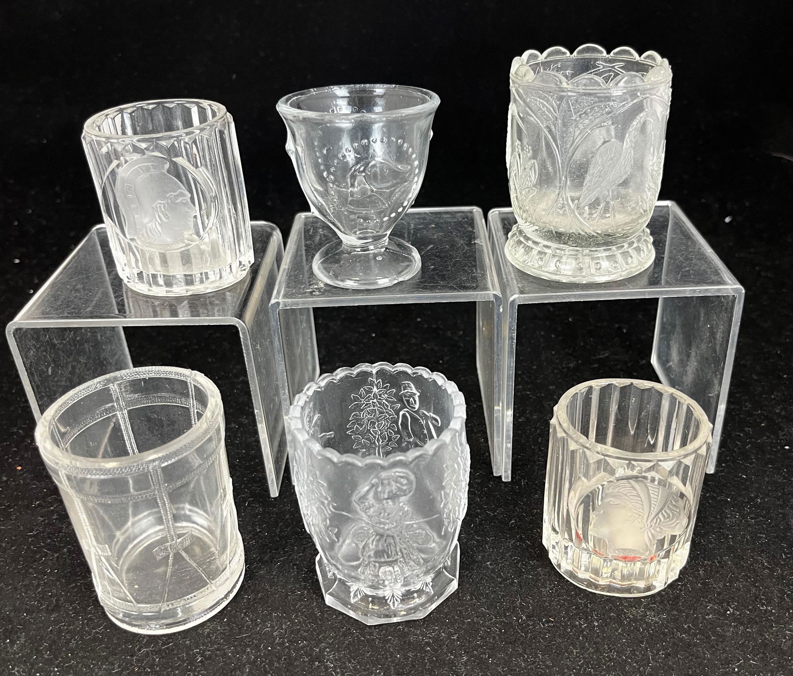 Six clear EAPG toothpick holders: Six unusual clear EAPG toothpick holders various makers and patterns, including Nursery Tales, Horse Head, Cameo of Diana, and Cameo of Apollo; tallest 2 5/8". CONDITION: good with minor wear.
