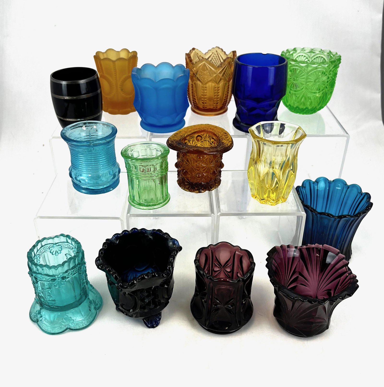 Grouping of 15 EAPG glass toothpicks: Grouping of 15 EAPG glass toothpick holders; assorted makers, patterns, and colors; tallest 2.5"; CONDITION: minor wear, cobalt with rim chip.