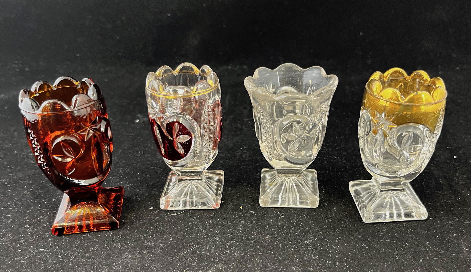 Four EAPG toothpick holders: Four Leaf and Star toothpick holders including three New Martinsville Glass one amber, one clear with gold dŽcor, one clear with ruby stain and a clear maker unknown; tallest 3". CONDITION: ruby stai