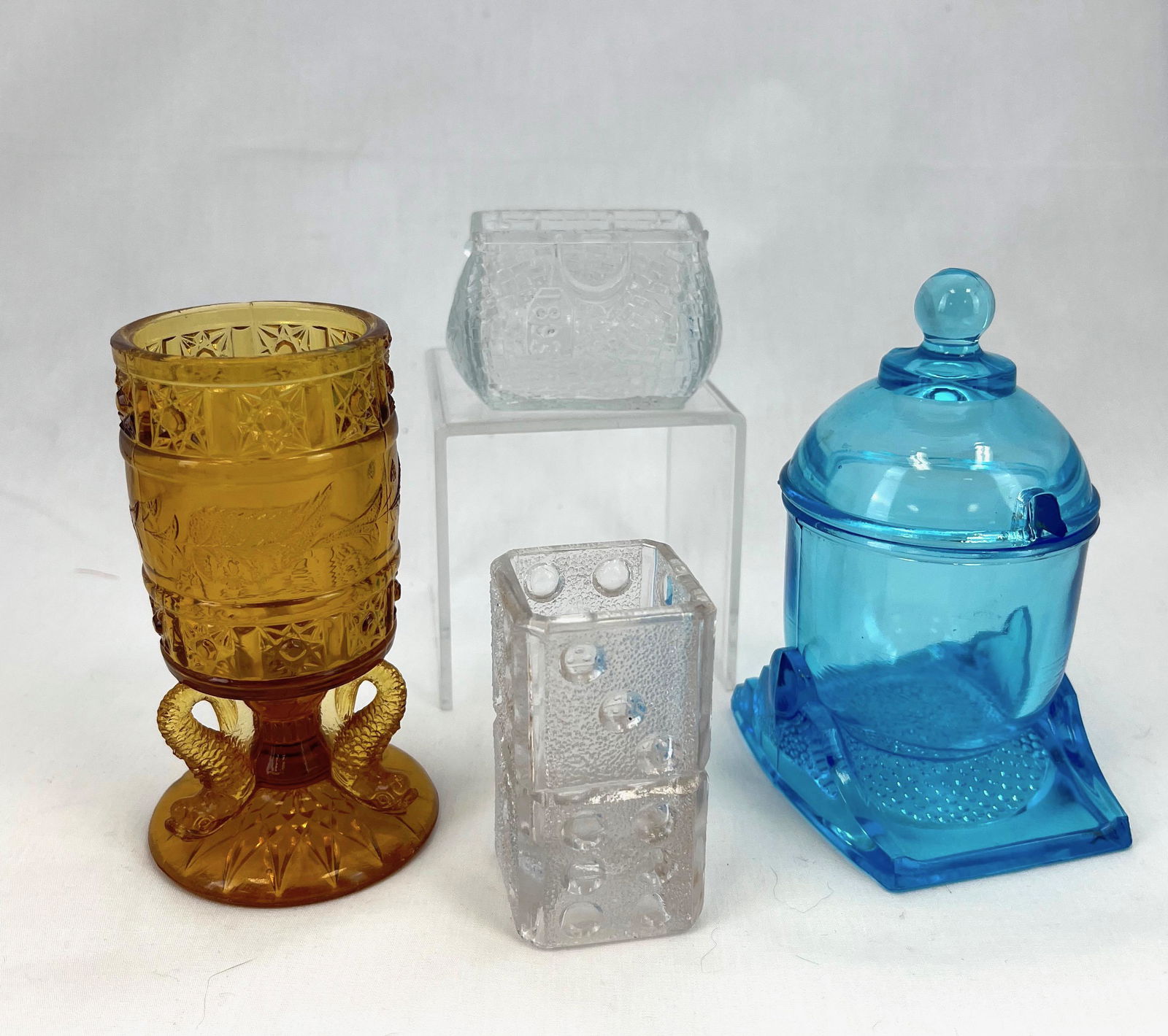 Four EAPG toothpick holders: Four EAPG toothpick holders including a clear Domino unknown maker, blue covered Gatlin Gun, an amber Dolphin match with three dolphins, and a clear Libby World's Fair Purse; tallest 4.5". CONDITION: