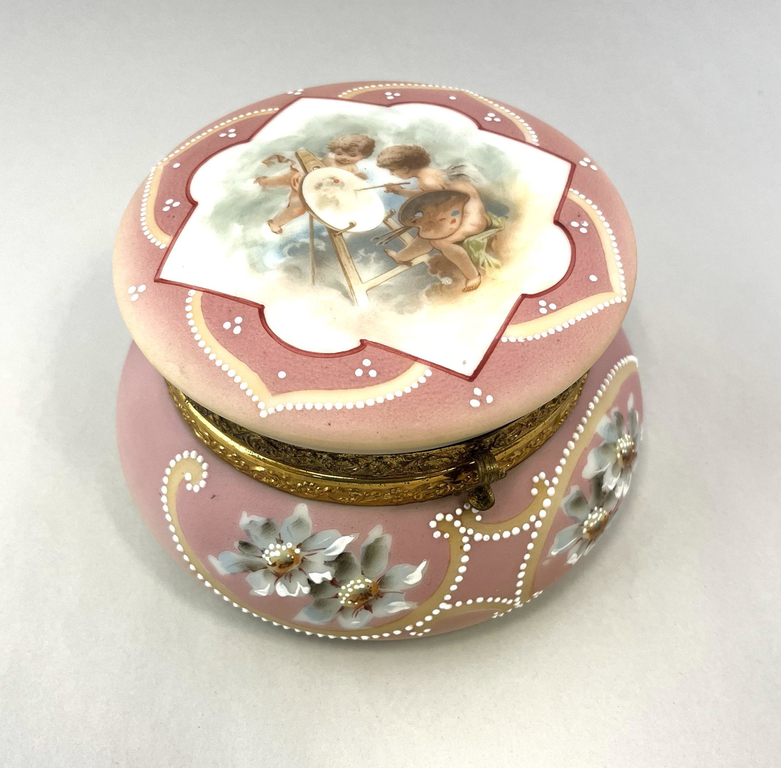 C. F. Monroe pictorial dresser box: Ovoid pink Nakara dresser box decorated with a central medallion of cherubs painting, a adorned with white dot scrolling and blue flowers, 5 1/2" wide. Condition: good with no defects found.