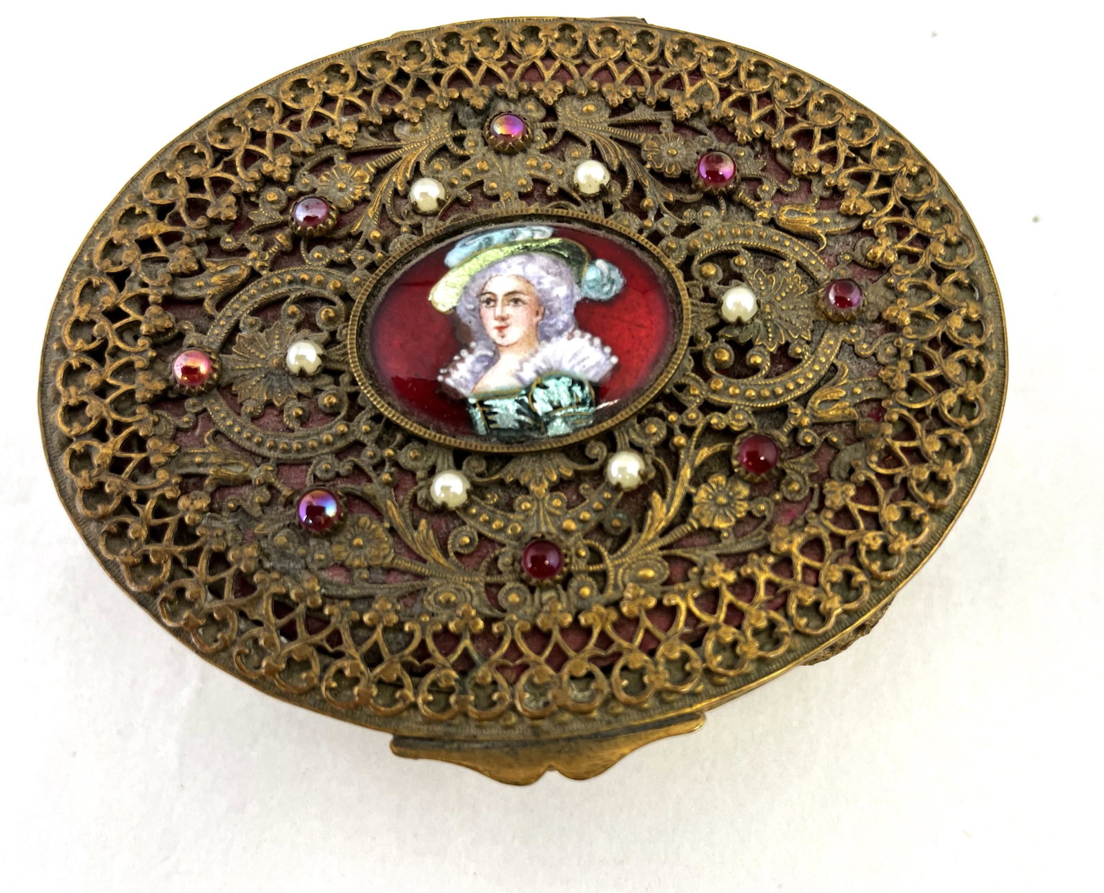 French filigree dresser box: Oval French dresser box with a central red medallion of a Continental Lady with an overall filigree and jeweled dŽcor, marked made in France, 4" long. CONDITION: Good with no issues.