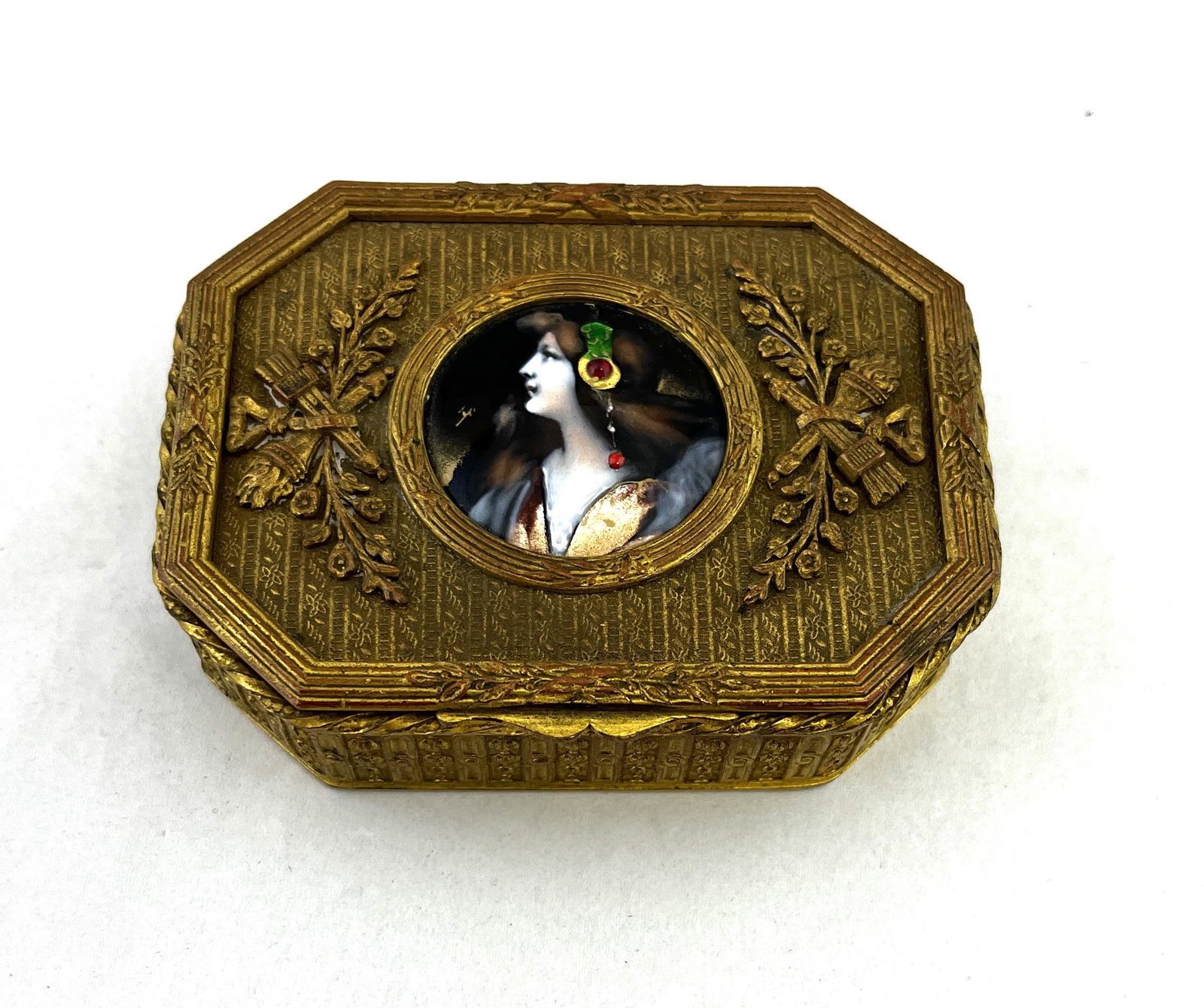 French metal dresser box: Metal dresser box with embossed flowers and ribbon decorated with a central medallion of an enameled Continental lady, marked Made in France, 3 1/2" long. CONDITION: Good with no issues.