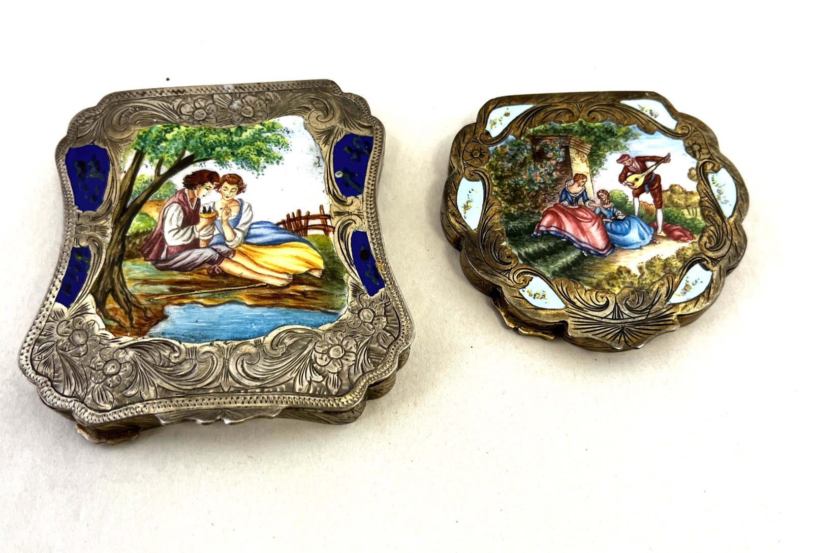 Two European silver enameled compacts: Two European silver compacts each with pictures of courting couples, one marked 900, largest 3 1/4" square. CONDITION: Good with no issues.