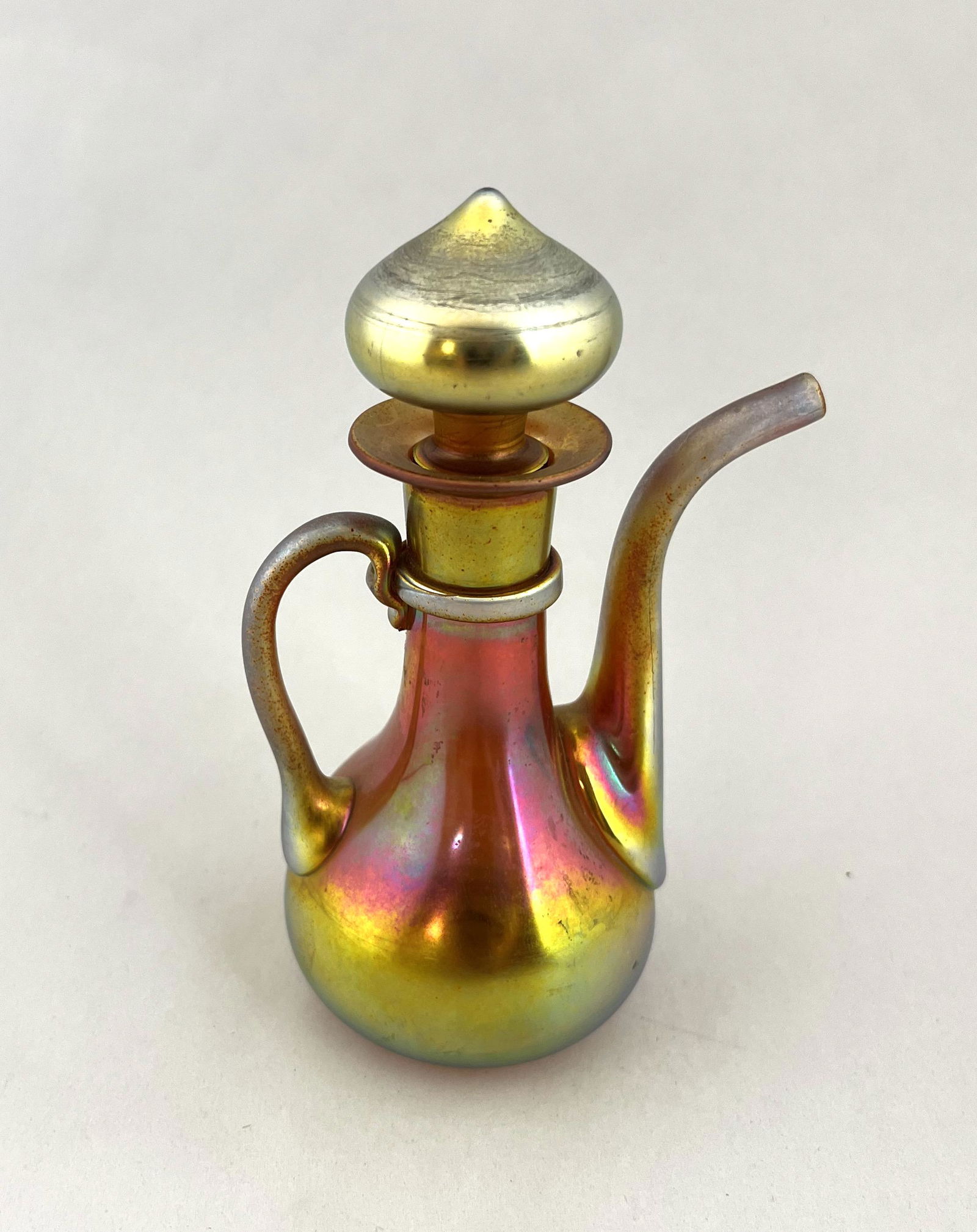 Steuben Gold Aurene cruet: Steuben Gold Aurene cruet with an applied handle and spout, adorn with a crown finial, signed Aurene 2720, 5 1/4" ht. CONDITION: good with no defects found.
