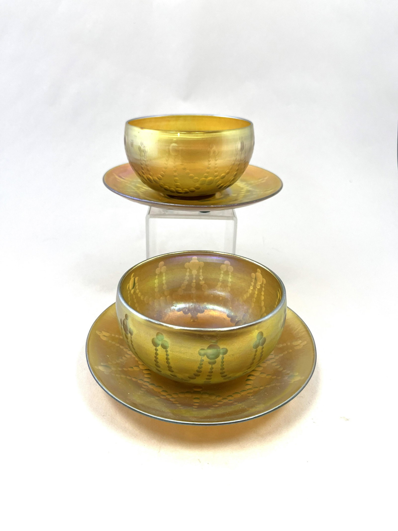 Pair of Tiffany finger bowls and plates: Pair of decorated Tiffany Gold Favrile finger bowls and underplate each with intaglio draped circles, all signed, 6" wide. CONDITION: good with no defects found.