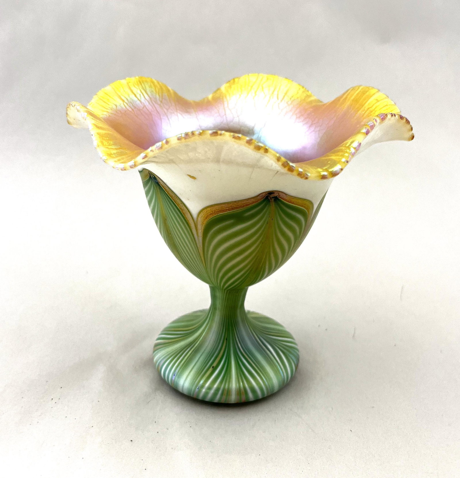 Quezal flower form glass vase: Footed Quezal flower form vase with a scalloped rim in opal glass with a green pulled feather tipped in gold, signed Quezal 274, 5" ht. CONDITION: good with no defects found.