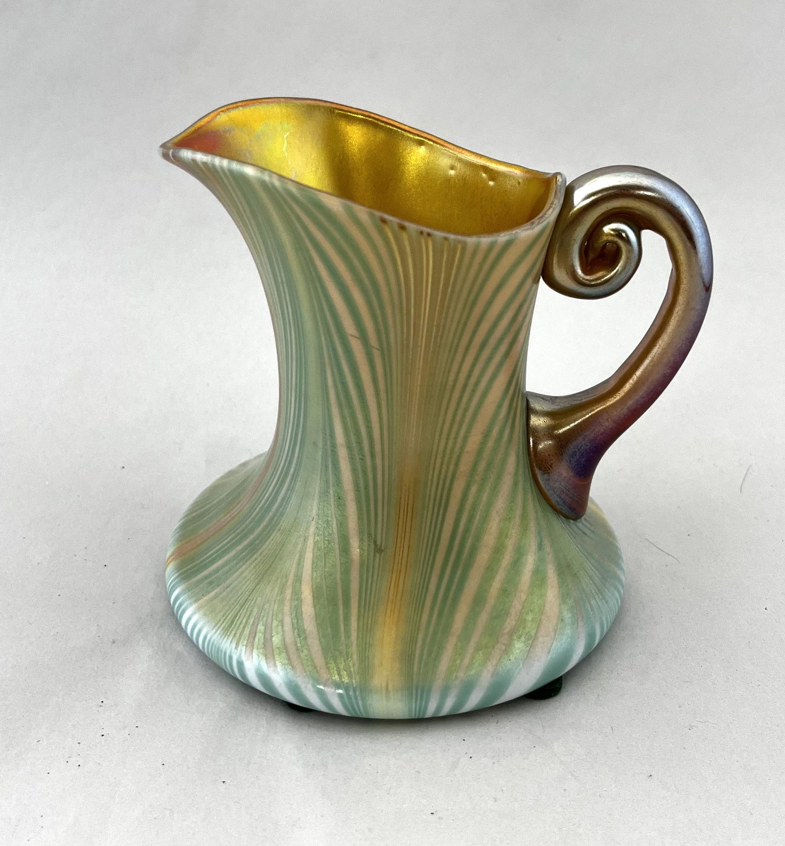 Kew Blas decorated pitcher: Kew Blas iridescent pitcher in marigold opal glass decorated with a green pulled feather and an iridescent gold handle, signed Kew Blas, 4 1/2' ht. CONDITION: good with no defects found.