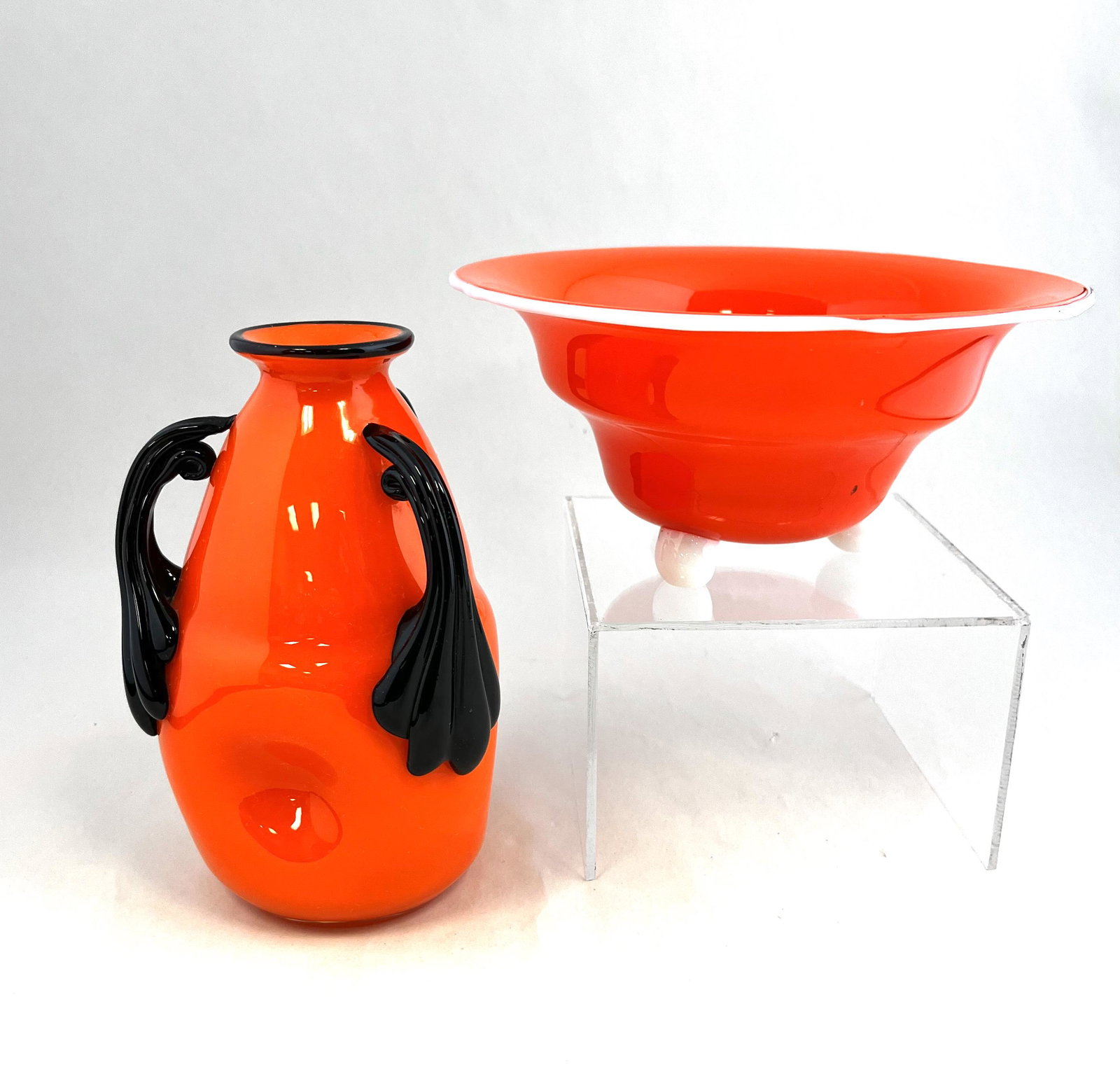 Two Loetz orange Tango glass vases: Two Loetz tango vases including a pinched sided orange with black handles together with an orange bowl with opal ball feet and lip wrap, tallest 6 1/2" ht. CONDITION: Good with no defects found