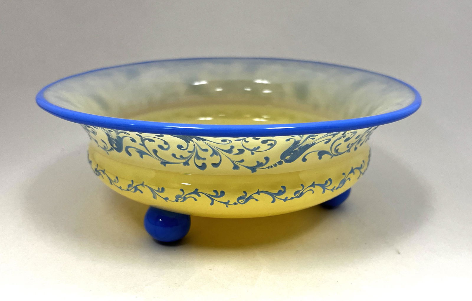 Loetz enameled glass compote: Loetz low cream colored compote with blue lip wrap and ball feet enameled with blue scrolling, 8 1/4" wide. PROVENANCE: Ernest Albanese. CONDITION: Good with no defects found.