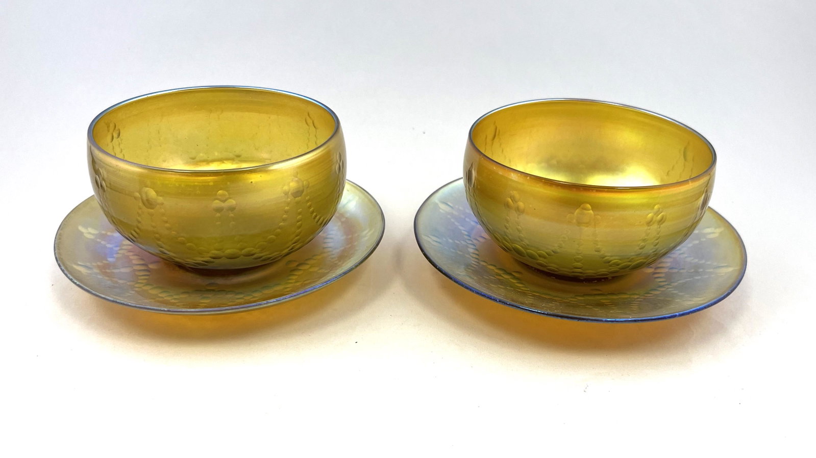 Pair of Tiffany intaglio finger bowls: Pair of Tiffany Gold Favrile finger bowls and underplates each with intaglio dotted swags, each marked L. C. Tiffany Favrile, 5 3/4" wide. CONDITION: Good with no defects found