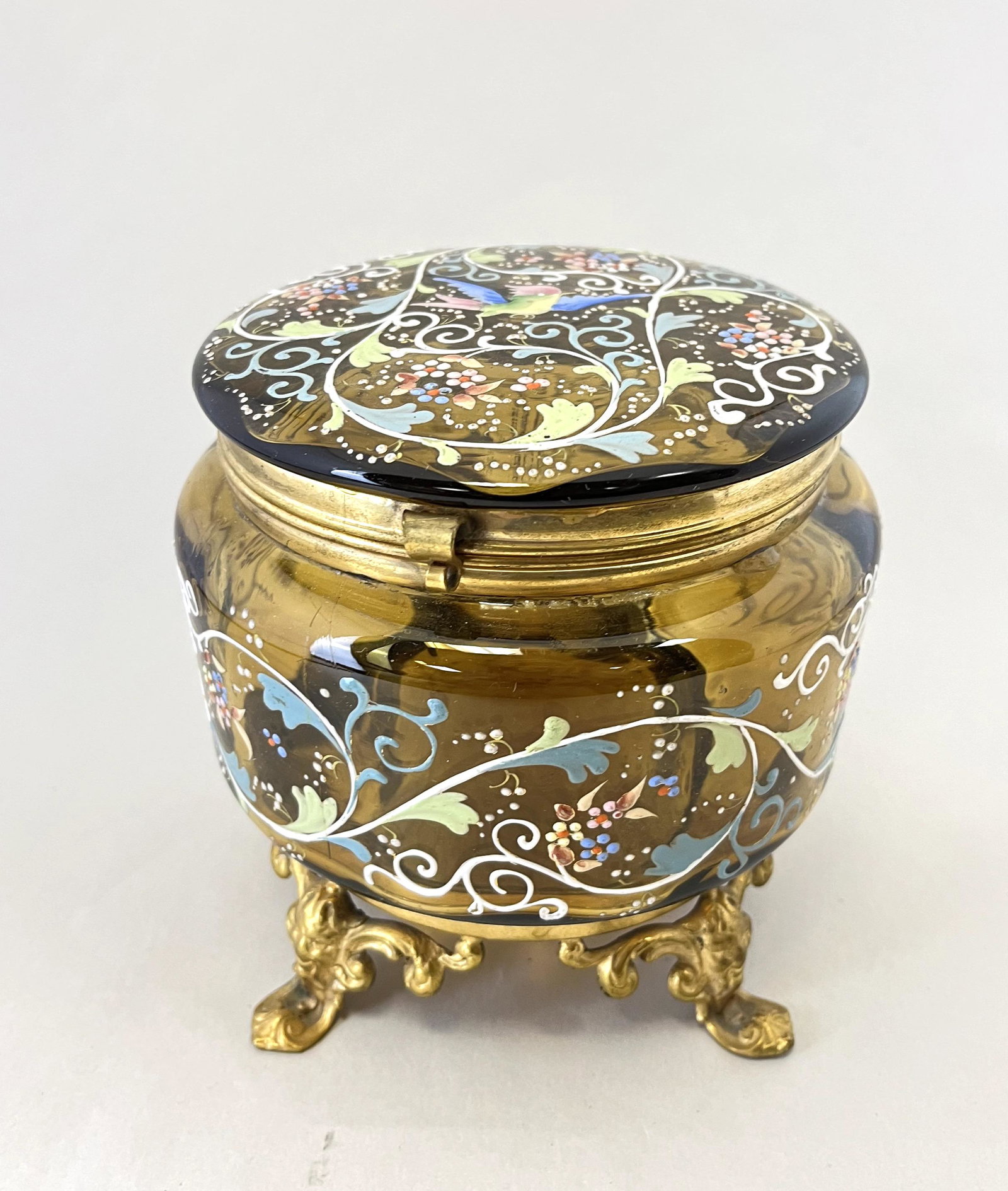 Amber enameled glass dresser box: Amber ovoid dresser box decorated with overall colorful scrolling and a central bird fitted with four mask feet, 5 1/4" ht. CONDITION: Good with no defects found