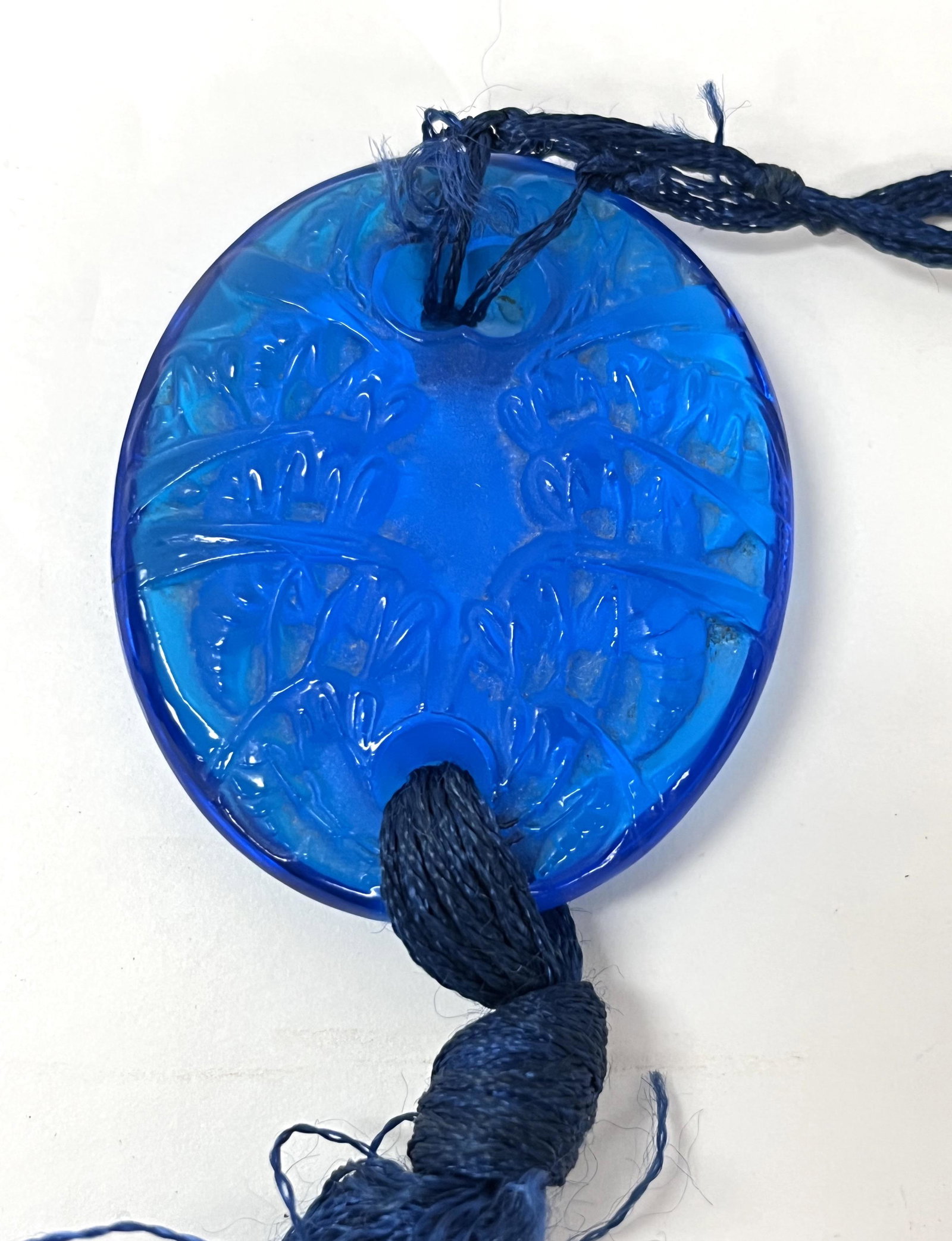 Lalique blue brooch: Lalique blue brooch with embossed dŽcor, signed Lalique; 2 1/4" oval with cord and tassel. CONDITION: no chips, cracks, repairs or material defects found. Jaremos attempts to call any material flaw t