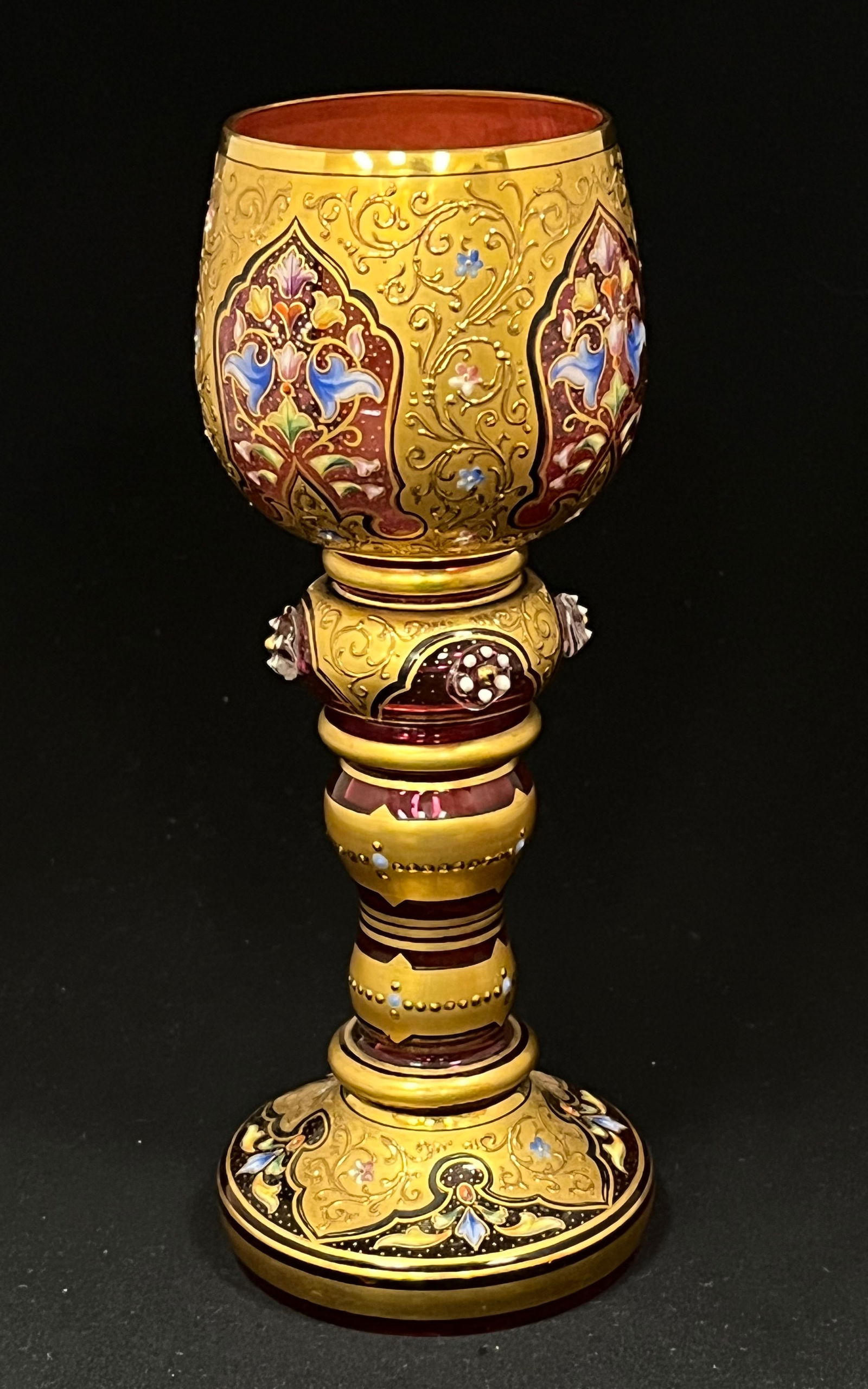 Moser enameled cranberry wine: Moser cranberry and gold encrusted goblet with church windows decorated with scrolling flowers adorned with four side cabachons, 7 1/2" ht. CONDITION: no chips, cracks, repairs or material defects fou