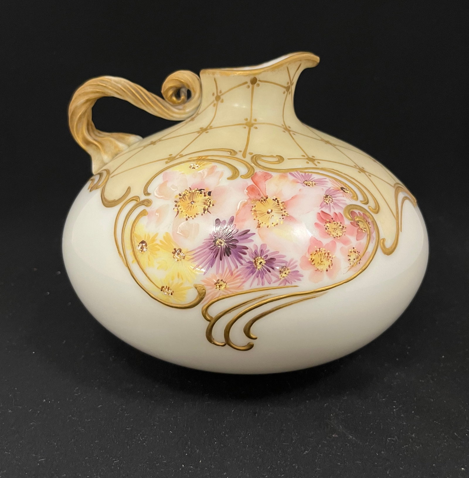 Mt. Washington glossy Crown Milano jug: Mt. Washington glossy Crown Milano ovoid jug in opal glass decorated with a yellow shoulder of gold lattice and flower medallions, reeded handle, marked with the factory backstamp 7" wide by 6" ht. CO