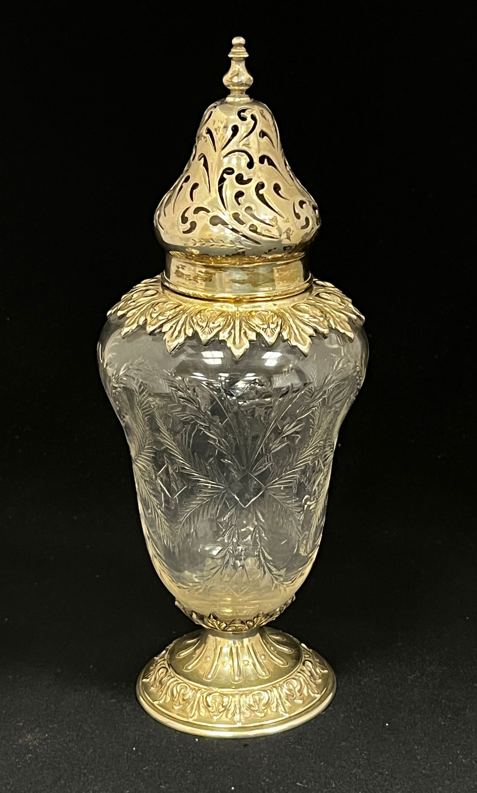 Cut glass and sterling sugar shaker: Cut glass sugar shaker with sterling silver pierced top and embossed foot with leaf and fern etching, 8 1/2" ht. CONDITION: no chips, cracks, repairs or material defects found, Jaremos attempts to cal