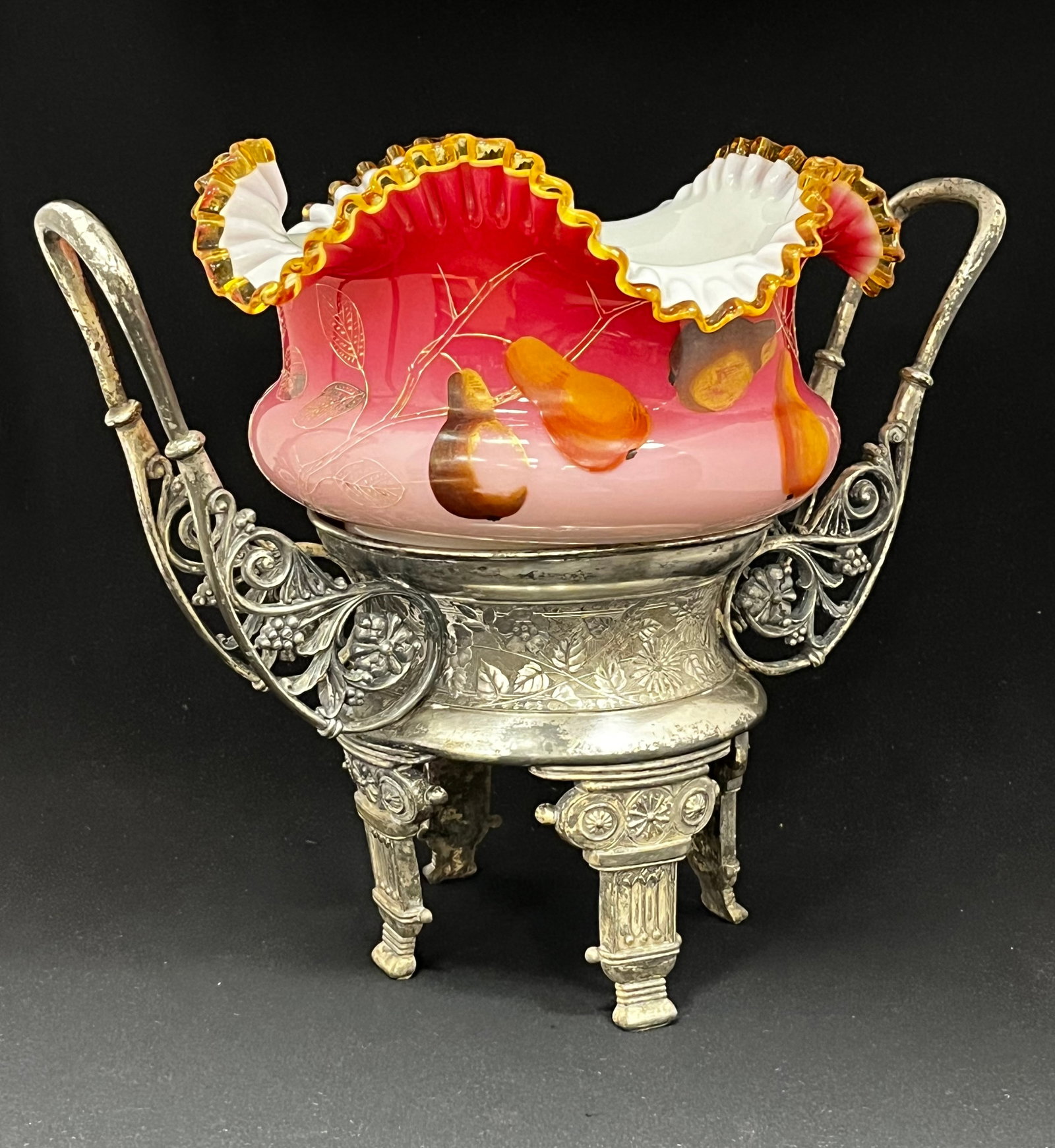 Peachblow Brides bowl and stand: Peachblow ruffled rim cased brides bowl with enameled pears set on a four footed Roger Smith two handle caddy, 11" ht. CONDITION: stand and bowl is a marriage, no chips, cracks, repairs or material de