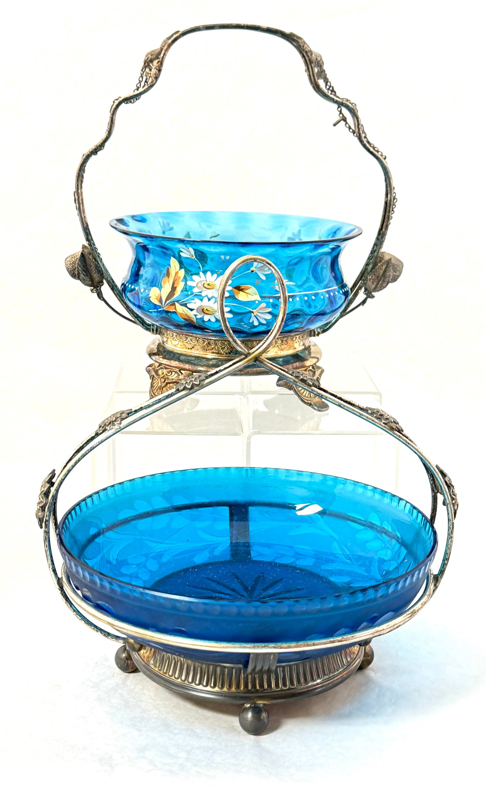 2 Prussian Blue Bride's Baskets: A Pairpoint cut signed holder with Prussian blue bowl together with a Prussian blue bowl with enameled flowers in a metal holder; tallest 10". CONDITION: no chips, cracks, repairs or material defects