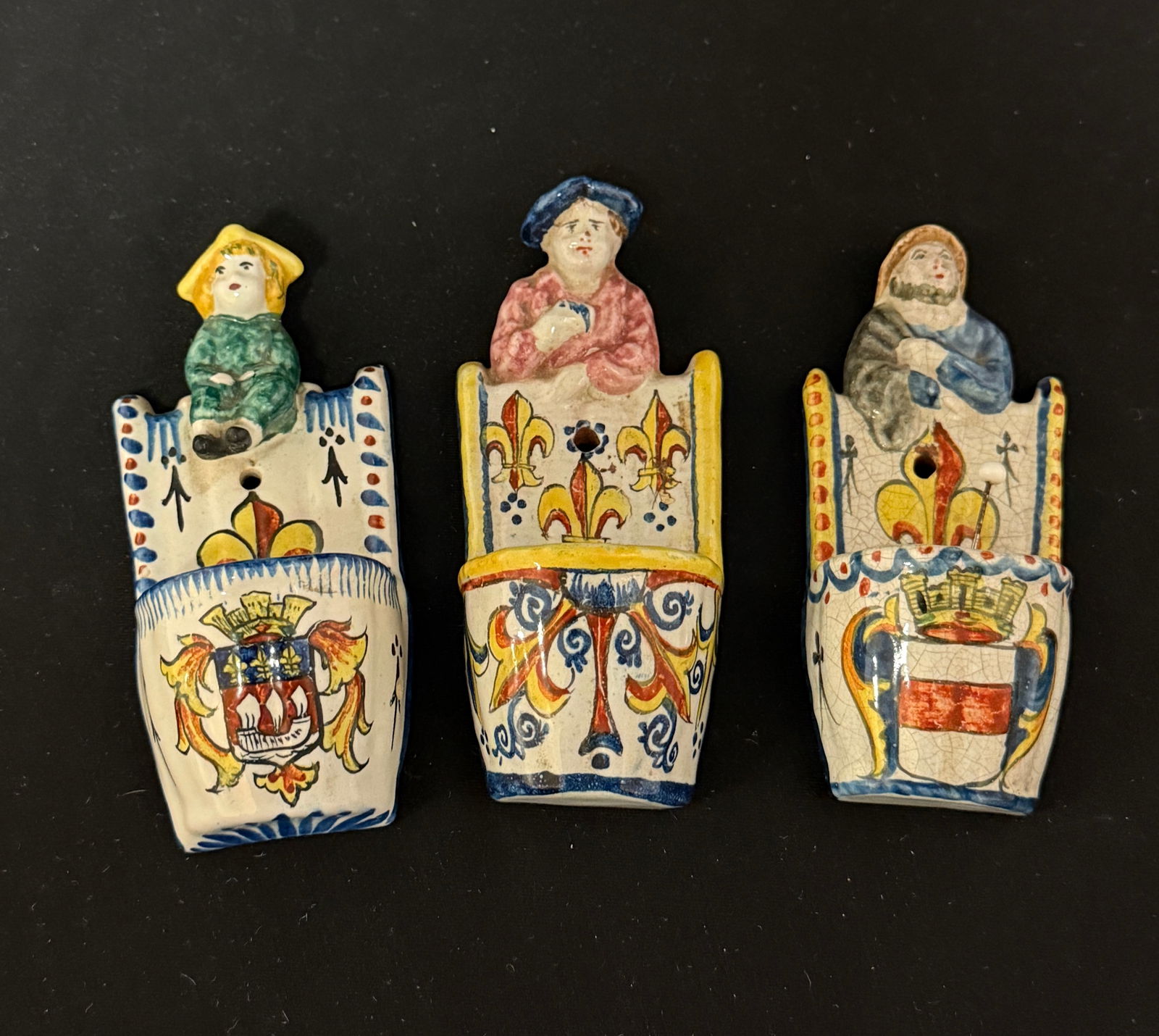 3 Alcide Chaumeil Pin Cushions: 3 Alcide Chaumeil (CA) wall mount pin cushions, a fisherman, a Breton, and a young boy all with fleur de lis motifs; largest 5". c. 184-1919. CONDITION: Quimper has propensity to have minor chips, gla