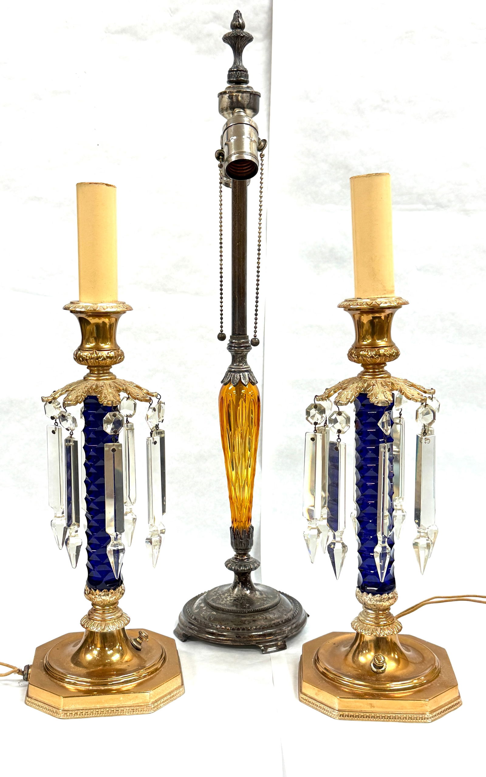3 Pairpoint Glass Candle Lamps: 3 Pairpoint glass candle lamps one amber needs wiring, 2 blue with prisms in working order but one is missing a prism; tallest 24 1/2". CONDITION: 1 prism missing on blue and amber needs electrified.