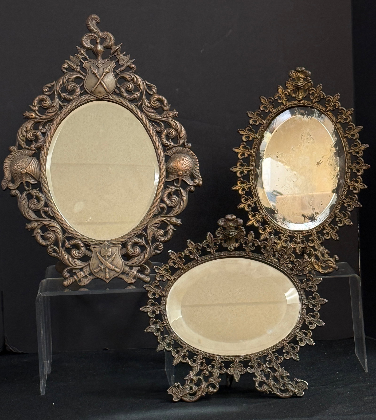 Three Victorian Stand Up Mirrors: Three Victorian reticulated metal stand up mirrors 2 with Fleur-de-Lis frames and one with a shield border, tallest 10 1/2" wide. CONDITION: one mirror with wear.