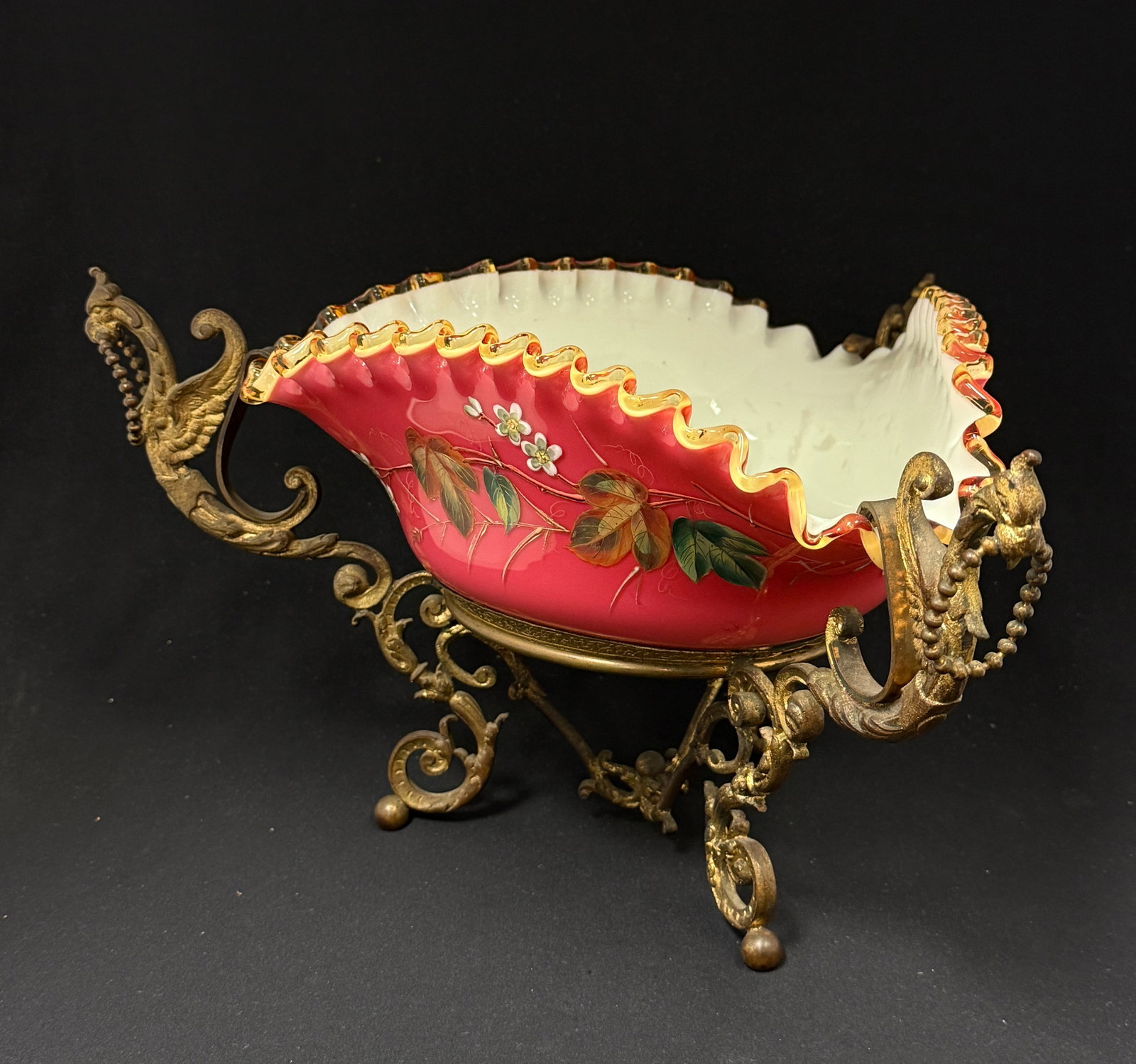 Webb Cased Ruby Bowl in Stand: Webb ruffled rim red triangular bowl with a cased interior decorated with enameled flowers and fitted with a griffin stand, 12" diameter. CONDITION: no chips, cracks, repairs, or material defects