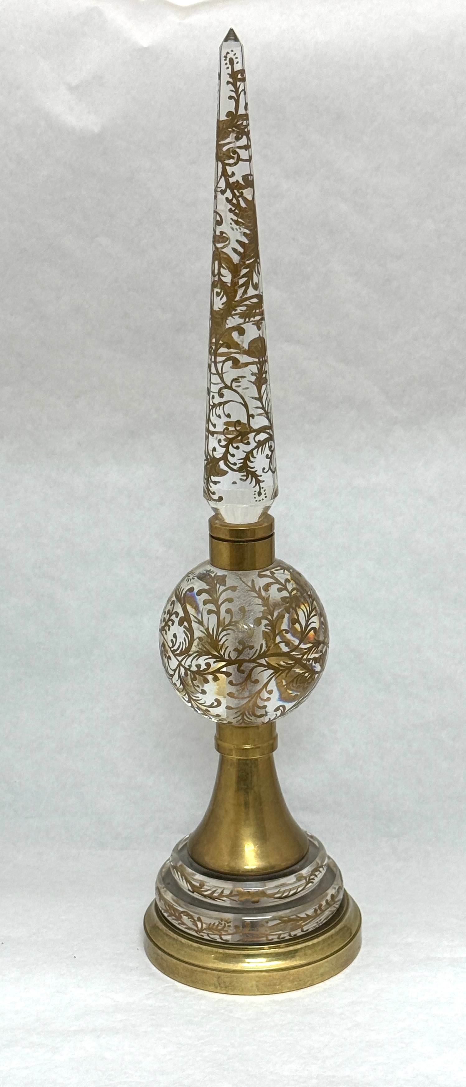 Glass and Brass Oblisk: Glass and brass obelisk with gold scrolling enamel; ht. 22". CONDITION: no chips, cracks, repairs, or material defects found, Jaremos attempts to call any material flaw that affects the price, but