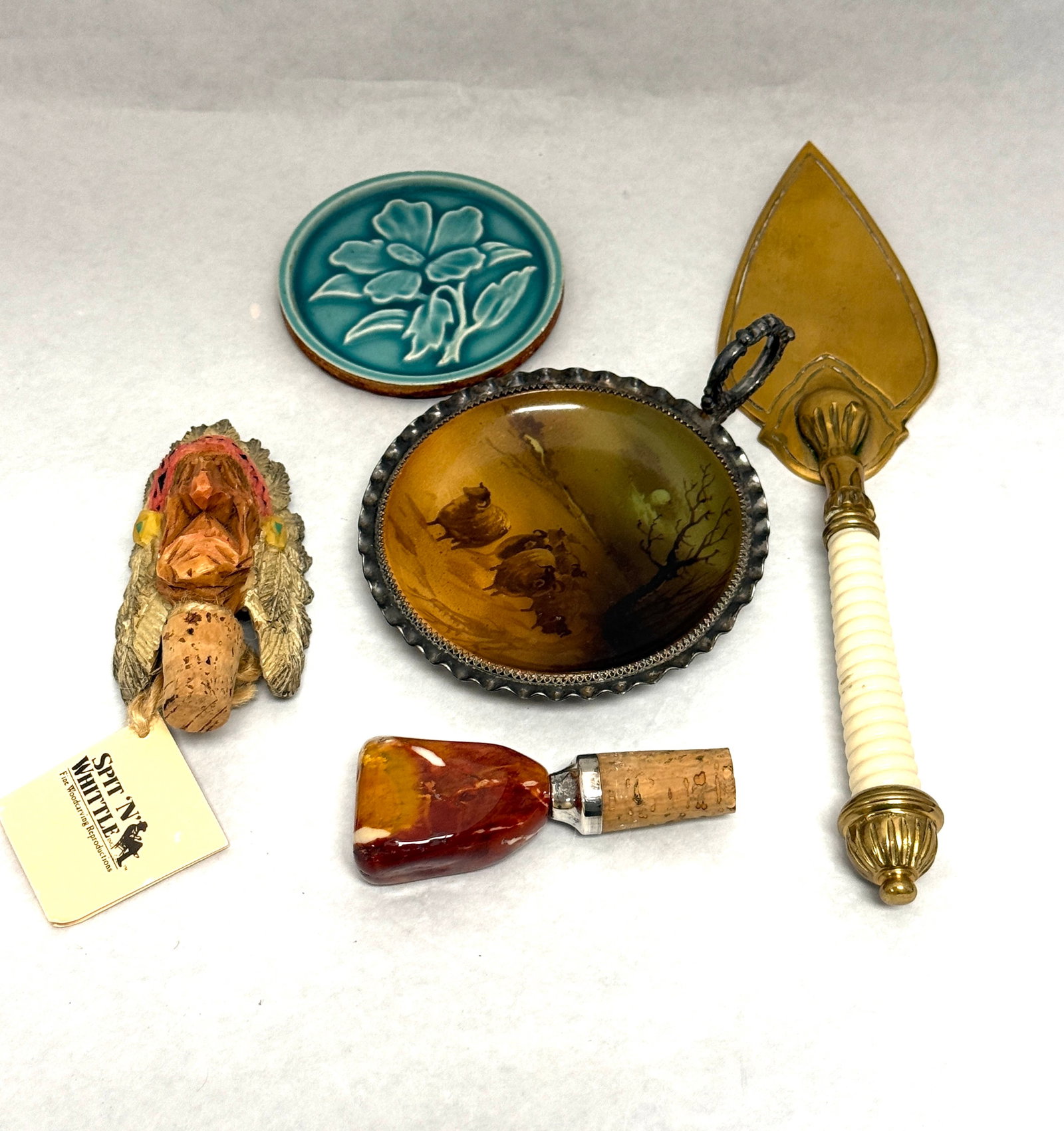 Group of decorative Items: Group of decorative items including a pie server, 2 wine bottle stoppers, a Pairpoint metal tray with painted porcelain insert and a pottery flower medallion; pie server length 11 7/8". CONDITION: no 