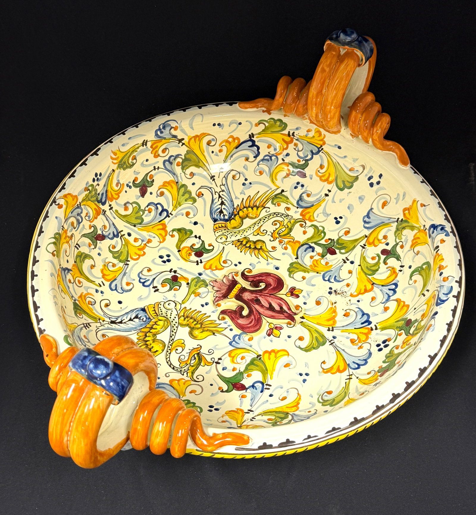 Large Deruta Center Bowl: Large Deruta 2 handle center bowl, purple Fleur de Lis in the center surround by blue, yellow and green leaf designs, signed Artistica Italy; diameter 20 1/2" with handles. CONDITION: no chips, cracks