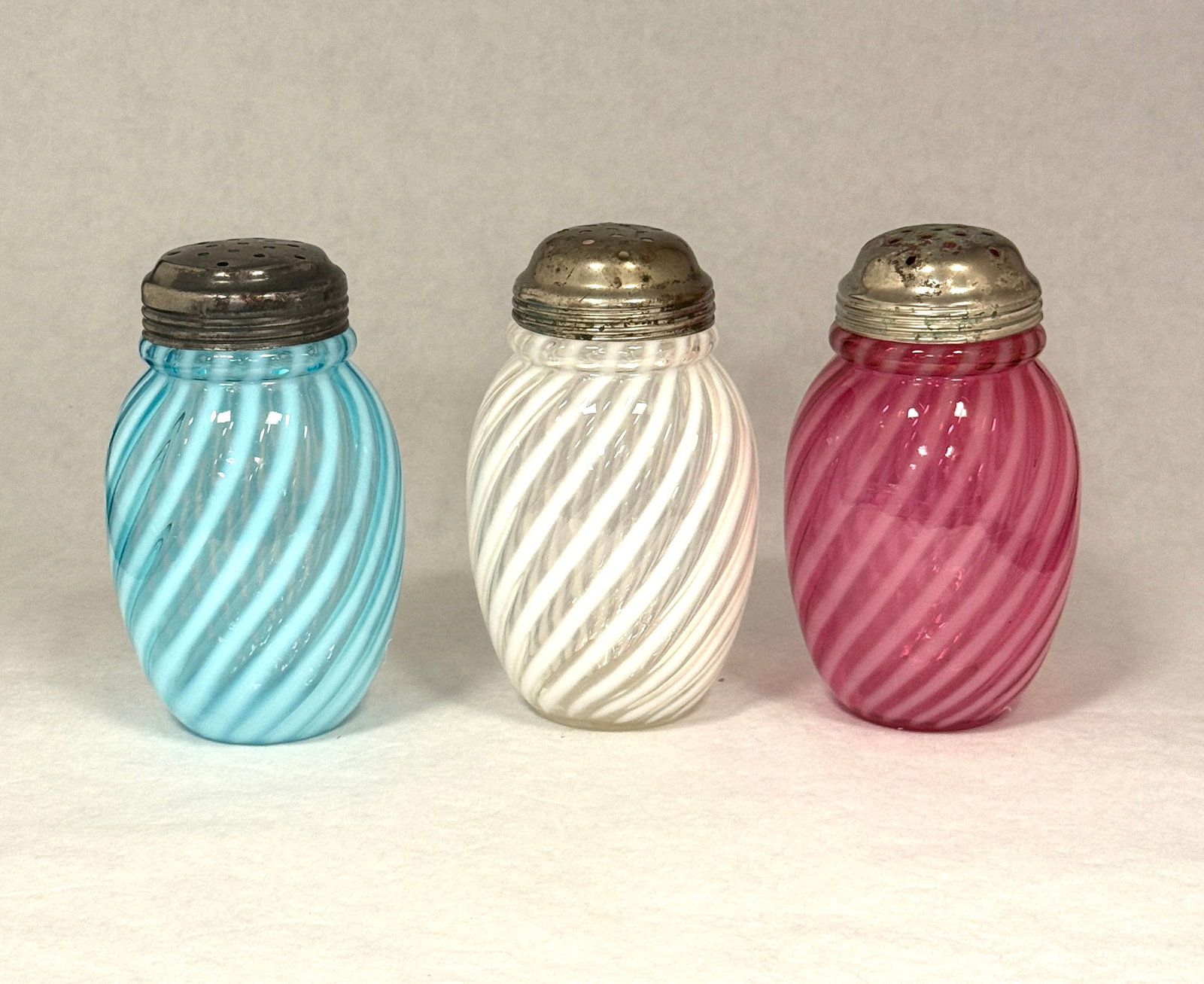 3 Opalescent Swirl Sugar Shakers: 3 opalescent swirl sugar shakers in white, blue, and cranberry; ht. 5". CONDITION: no chips, cracks, repairs, or material defects found, Jaremos attempts to call any material flaw that affects the pri